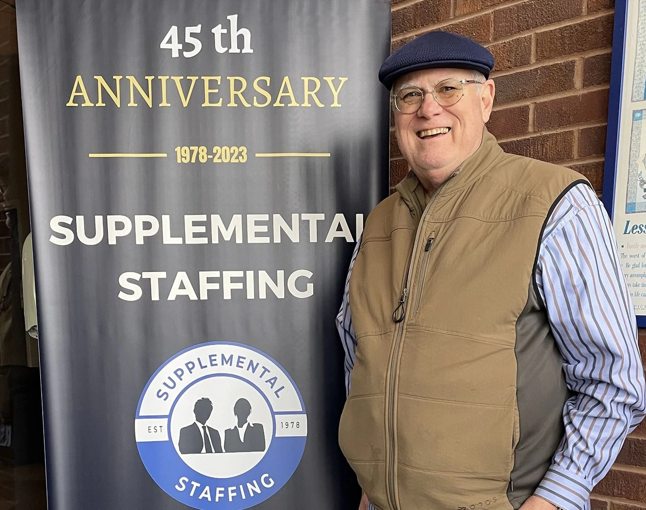 Malcolm Richards, standing next to Supplemental Staffing's 45th Anniversary sign